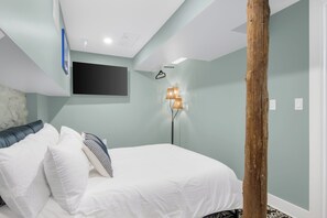 Ein Schlafzimmer mit einem Bett, Kissen, einem an der Wand montierten Fernseher und einer Stehlampe.