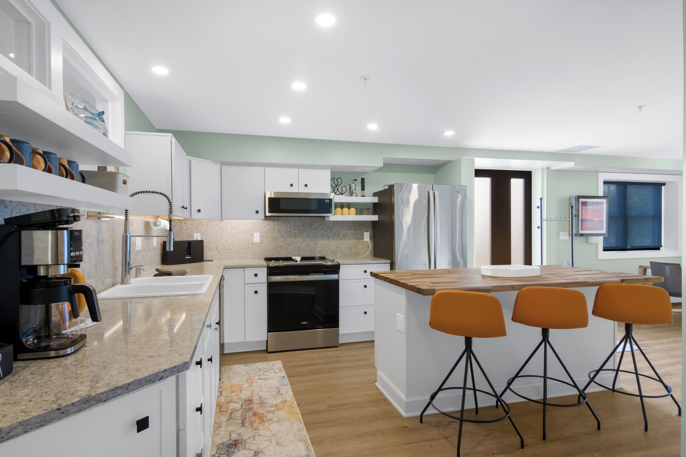 Une cuisine moderne avec des meubles blancs, un îlot central doté de tabourets, un four encastré, un four à micro-ondes et un réfrigérateur.
