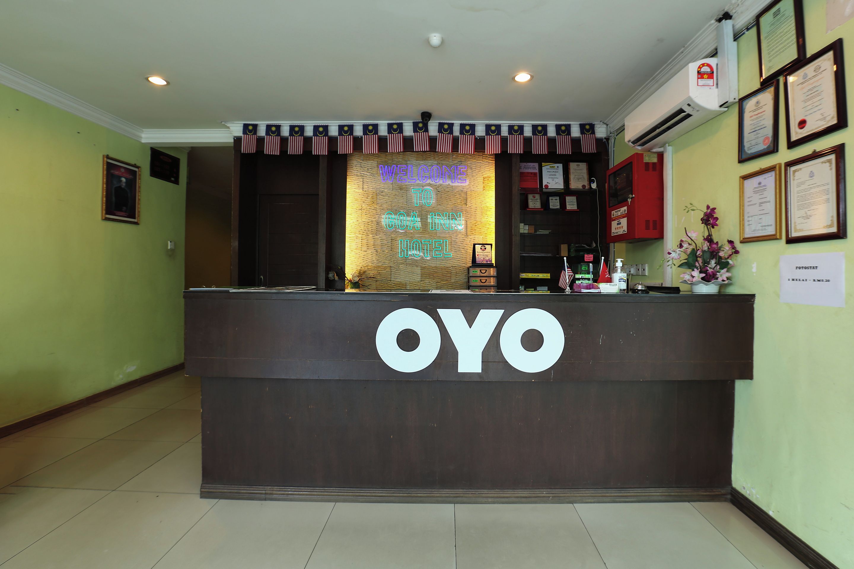 A reception desk with a neon sign reading 'Welcome to Goa Inn Hotel' and the name 'OYO' prominently displayed.