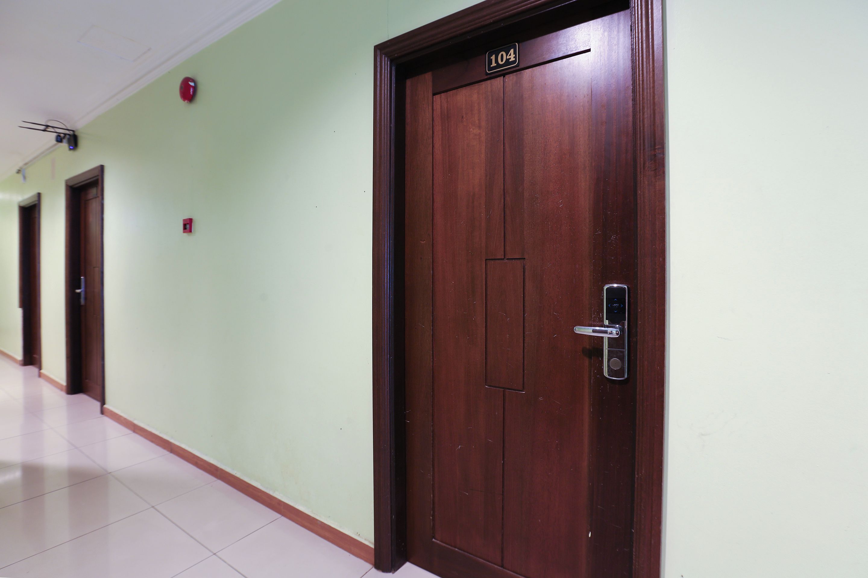 A hallway with a wooden door labeled '104' and a fire alarm on the wall.