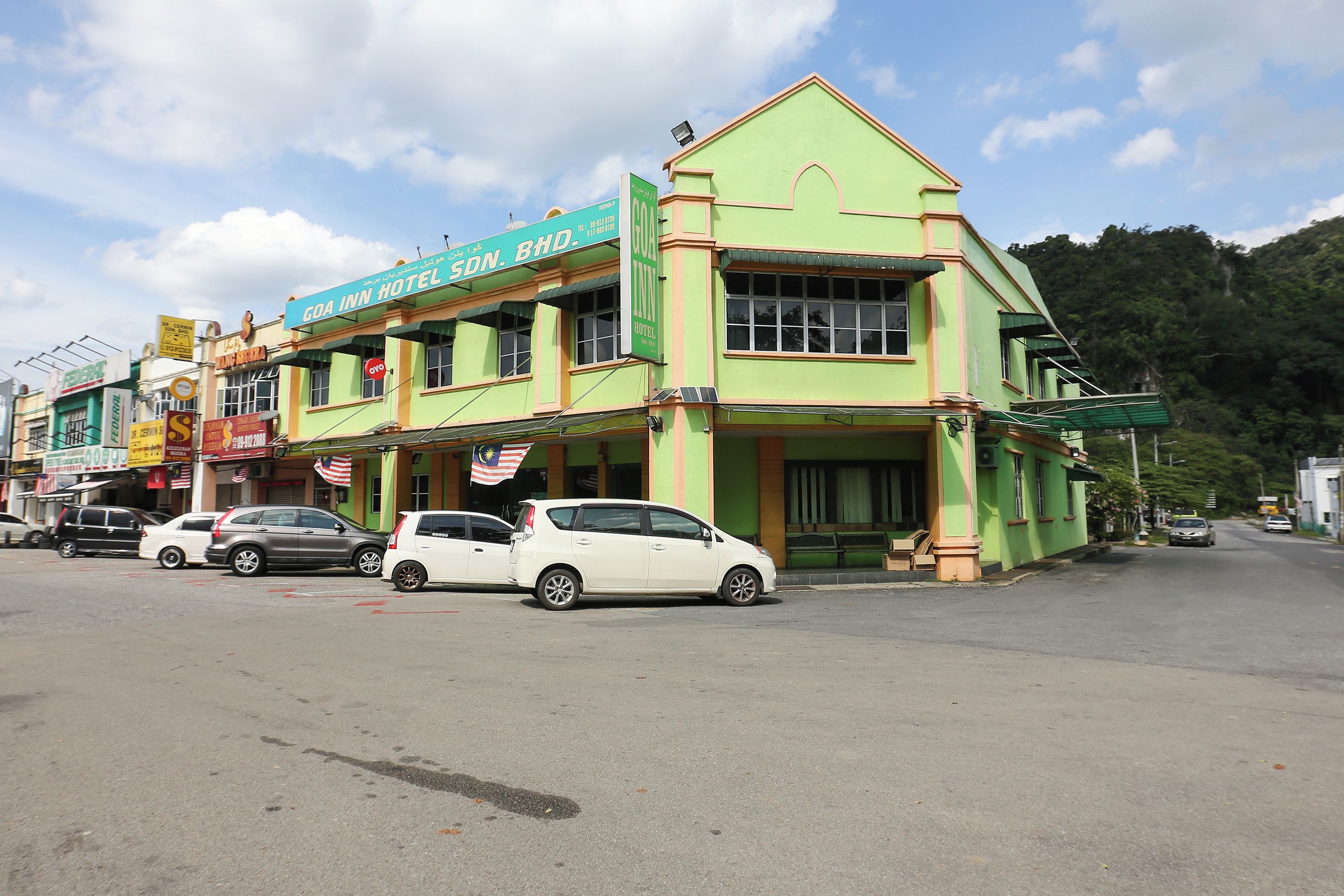 A hotel with a green facade, multiple windows, and a signboard.