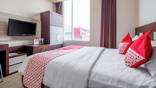 Ein Hotelzimmer mit Bett, Wandfernseher, Schreibtisch mit Schubladen und einem fenster mit Vorhängen.