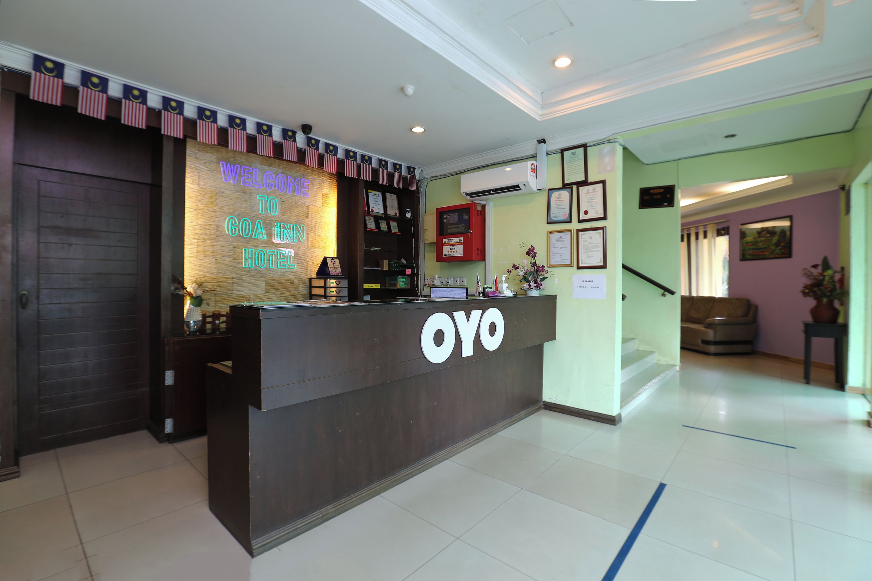 A hotel reception desk with a neon sign, a reception area, and a staircase leading to another floor.