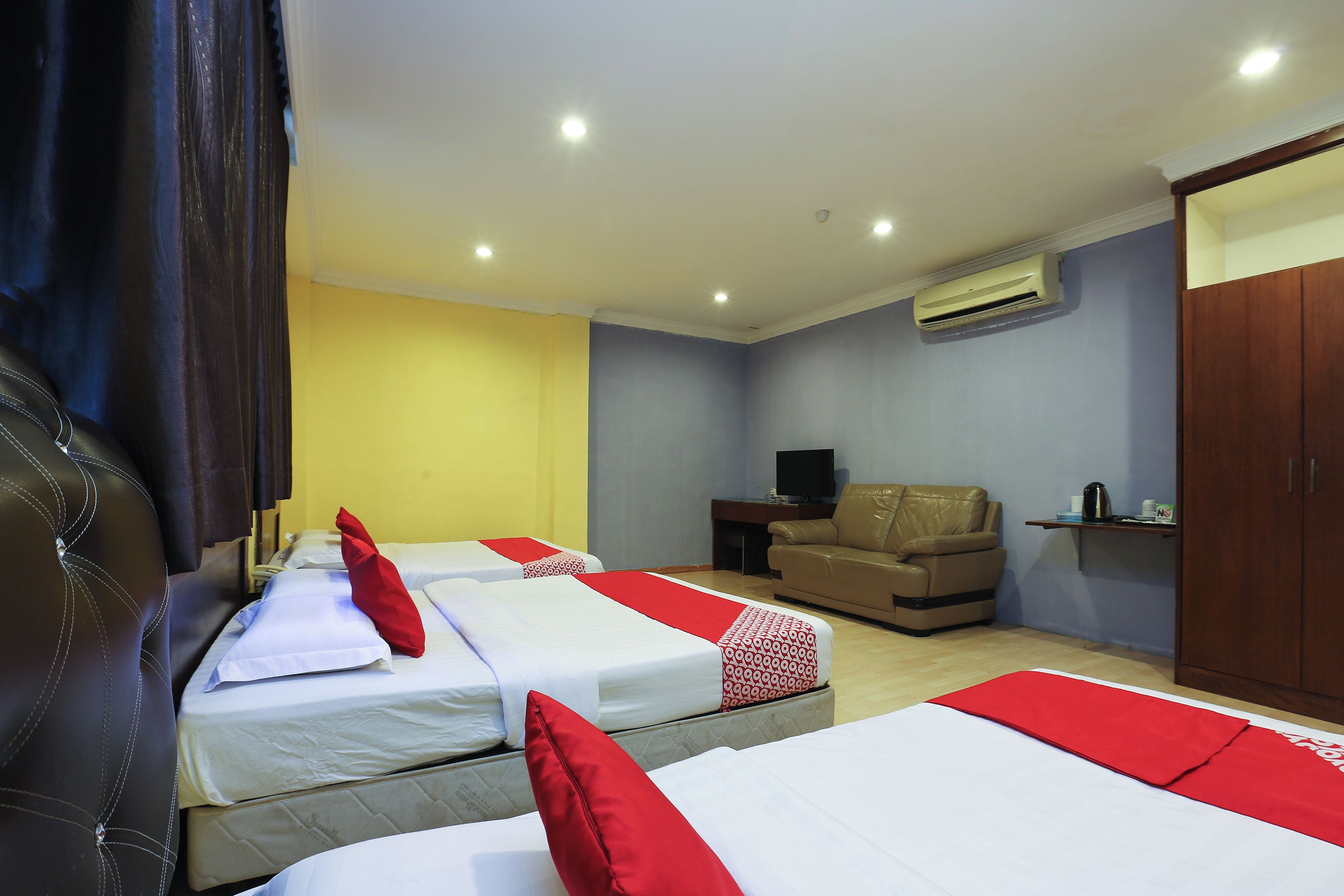 A hotel room with two beds, a sofa, a television, and an air conditioning unit.