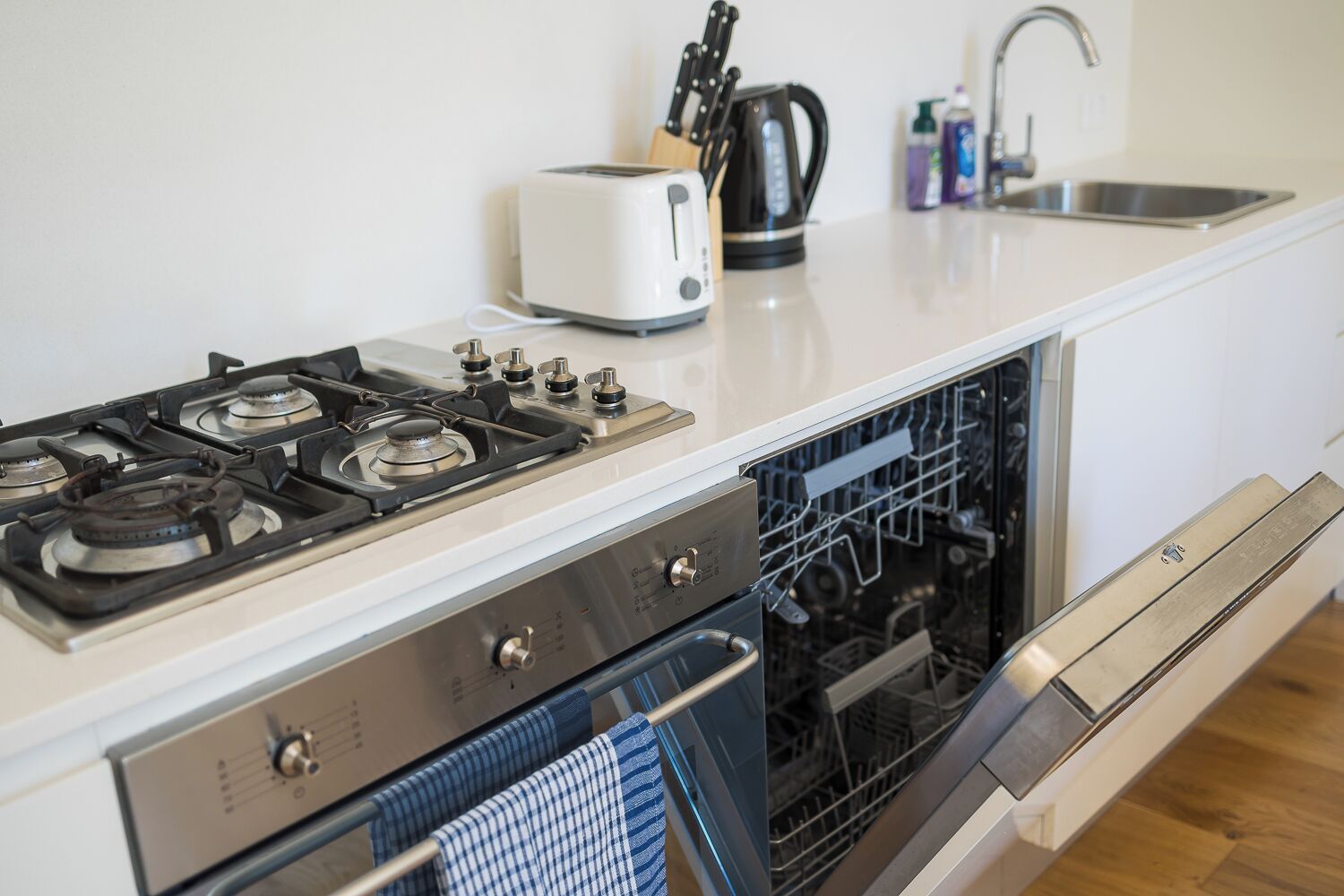 A kitchen with a gas stove, a toaster, a kettle, and a dishwasher.