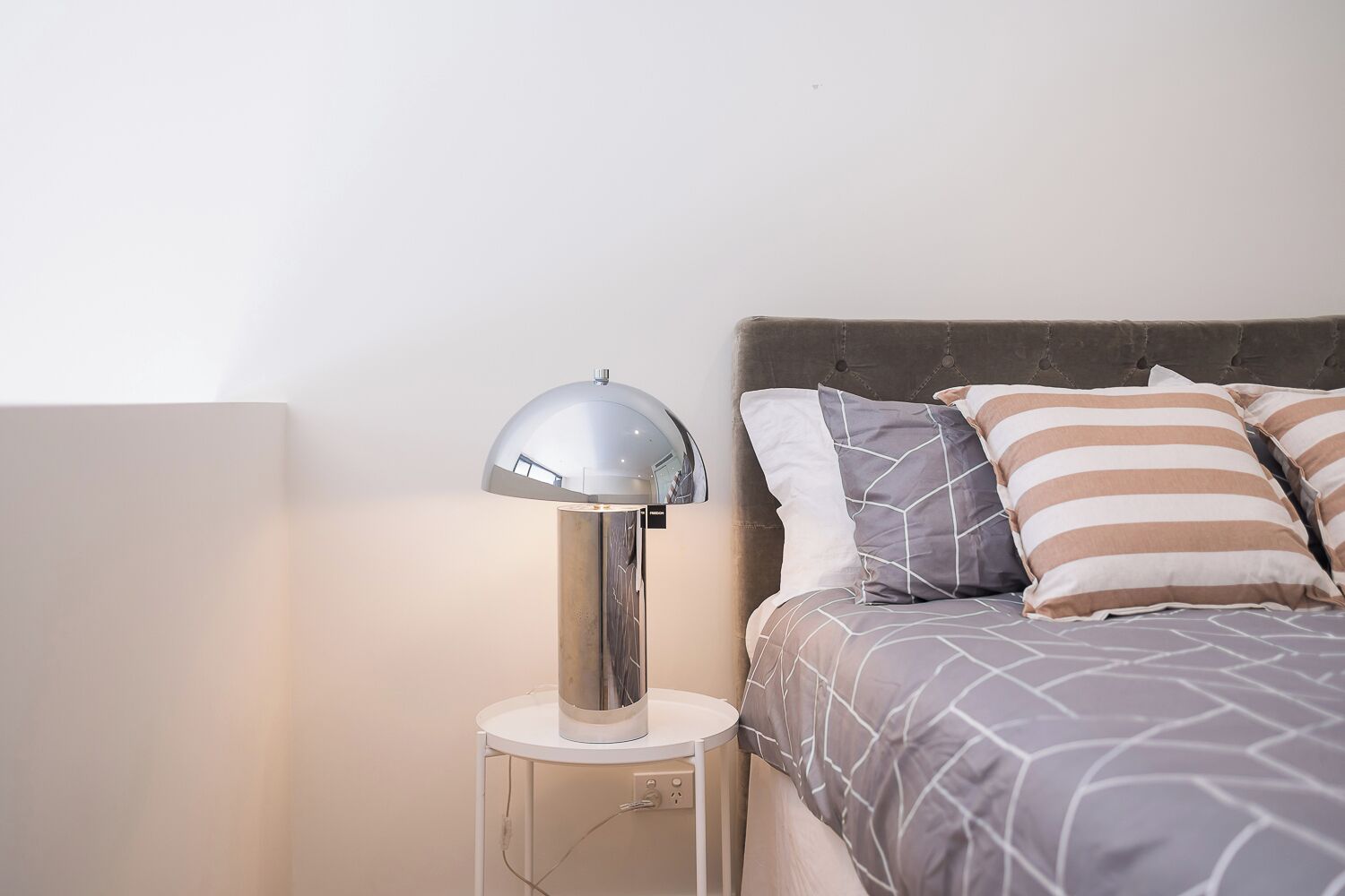 A bed with a grey and white patterned bedspread, a grey upholstered headboard, and striped pillows.