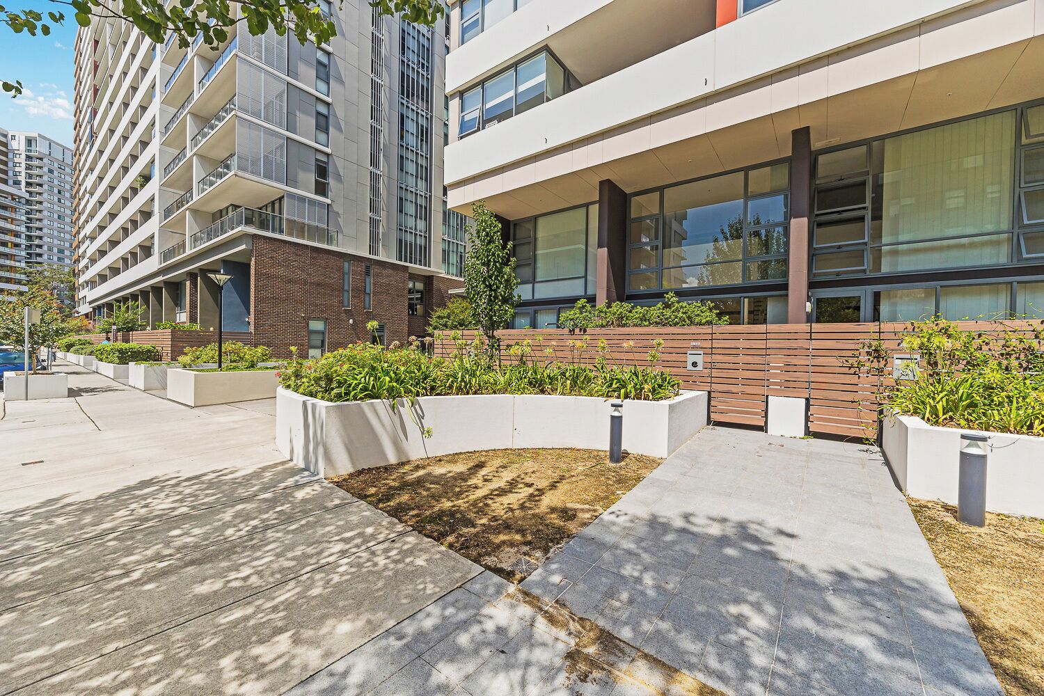 A modern building with a flat roof, large windows, and a landscaped area with planters and a wooden fence.