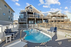 Uma área de piscina com deck de madeira, espreguiçadeiras e um edifício com varandas múltiplas.