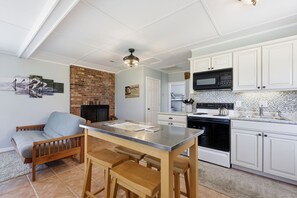 A modern kitchen with white cabinets, a black microwave, and a stove. There is a dining area with a wooden table and chairs. - Marshallberg Waterfront Cottage w/Dock! (Marshallberg)