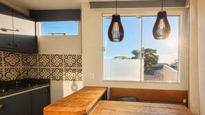 A compact kitchen with a wooden table, two hanging pendant lights, and a window with a view of the outside. - Loft Campeche 500mt da Praia - Floripa (Florianópolis)