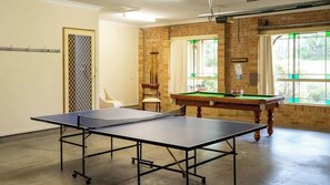 Una stanza con tavolo da ping pong, tavolo da biliardo, una sedia e una finestra con vista.