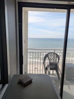 Ein Balkon mit Blick auf den Strand, ein Stuhl und ein Tisch mit einer Zeitschrift.