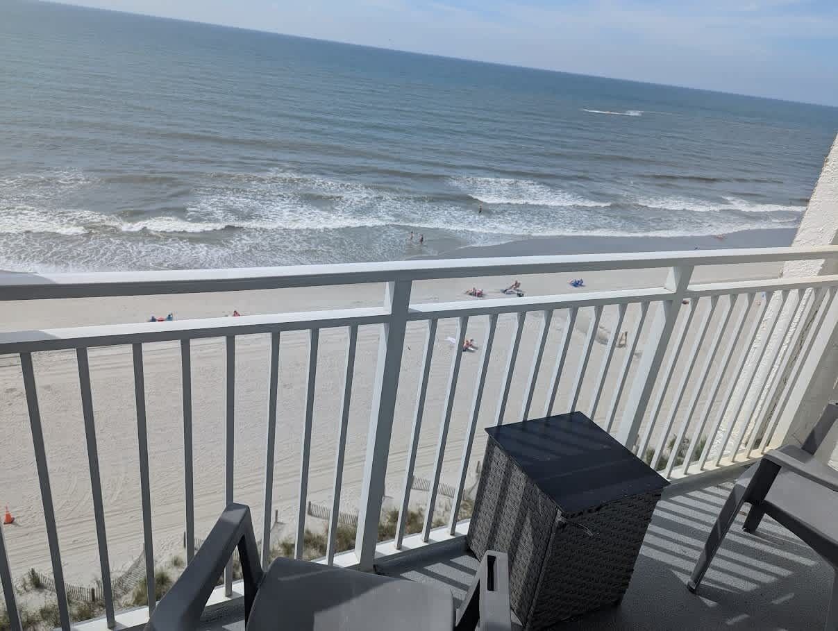 A balcony with a view of the ocean, a grill, and a chair.