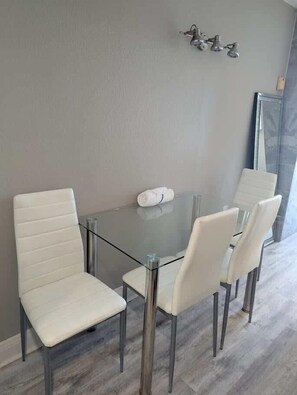 A modern dining area with a glass table and white upholstered chairs. - Sea Mist 20907 Newly Renovated Oceanfront Studio (Myrtle Beach)