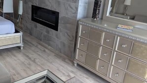 A modern bedroom with a bed, a dresser, a flat-screen TV mounted above a fireplace, and a large mirror. - Sea Mist 20907 Newly Renovated Oceanfront Studio (Myrtle Beach)