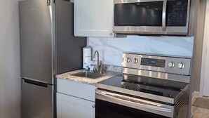 A compact kitchen with stainless steel appliances, including a refrigerator, microwave, and oven. - Sea Mist 20907 Newly Renovated Oceanfront Studio (Myrtle Beach)