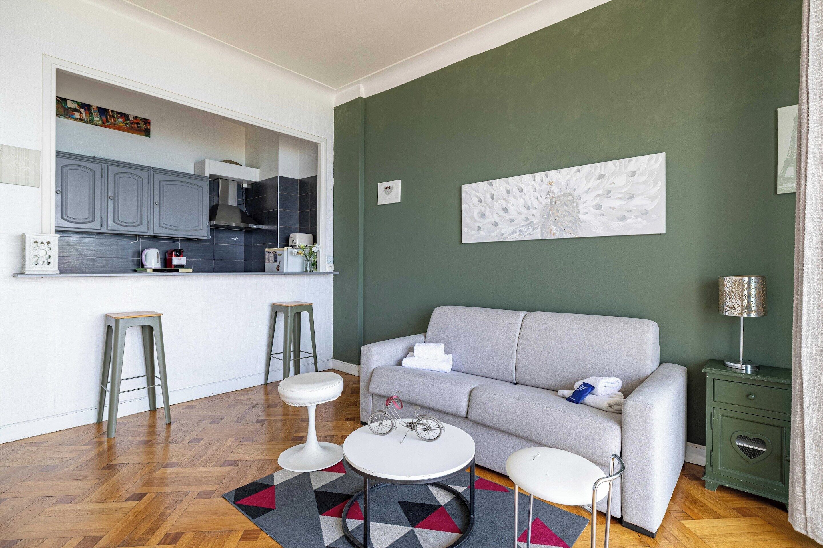 Una sala de estar moderna con un sofá gris, dos mesas redondas blancas, un tapete estampado y un aparador verde.