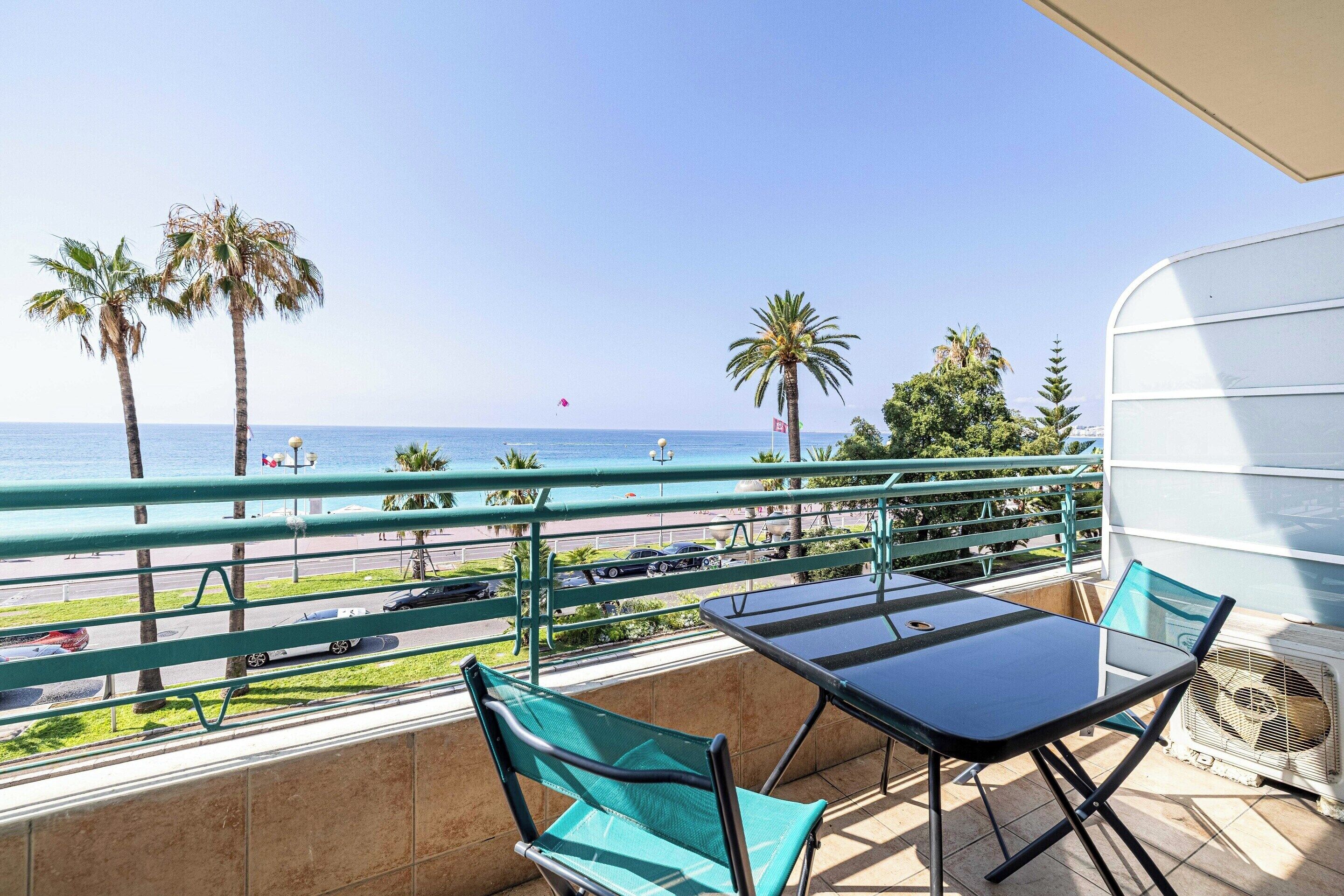 Un balcón con vistas al mar, una mesa, sillas y un ventilador.