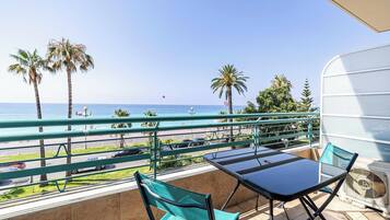 Un balcón con vistas al mar, una mesa, sillas y un ventilador.