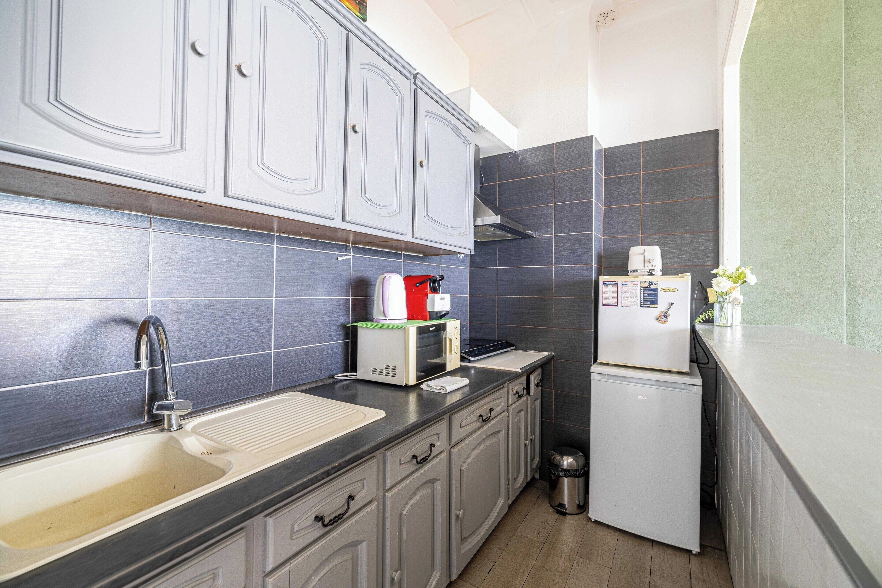 Cocina compacta con armarios grises, un lavamanos de acero inoxidable, un tostador, un hervidor y un refrigerador pequeño.