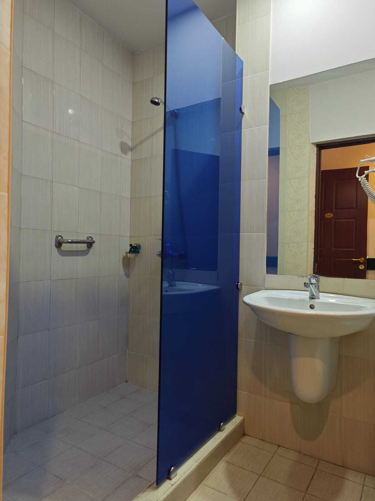 Un baño con cabina de ducha de vidrio, un lavabo blanco y una puerta que da a otra habitación.