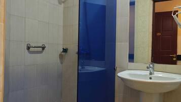 Un baño con cabina de ducha de vidrio, un lavabo blanco y una puerta que da a otra habitación.