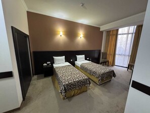 A hotel room with two beds, a dark headboard, bedside tables, a window with curtains, and a ceiling light. - Canyon Hills Hotel (Yerevan)