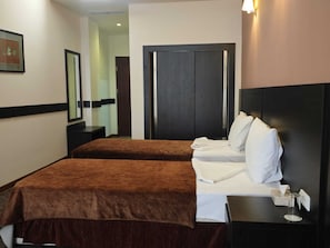 A hotel room with two beds, a dark wooden wardrobe, a bedside table with a lamp, and a framed picture on the wall. - Canyon Hills Hotel (Yerevan)