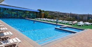 A swimming pool with lounge chairs and a stone wall. - Canyon Hills Hotel (Yerevan)