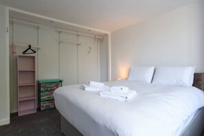Un dormitorio con una cama bien hecha, un armario con espacio para colgar y un pequeño baúl.