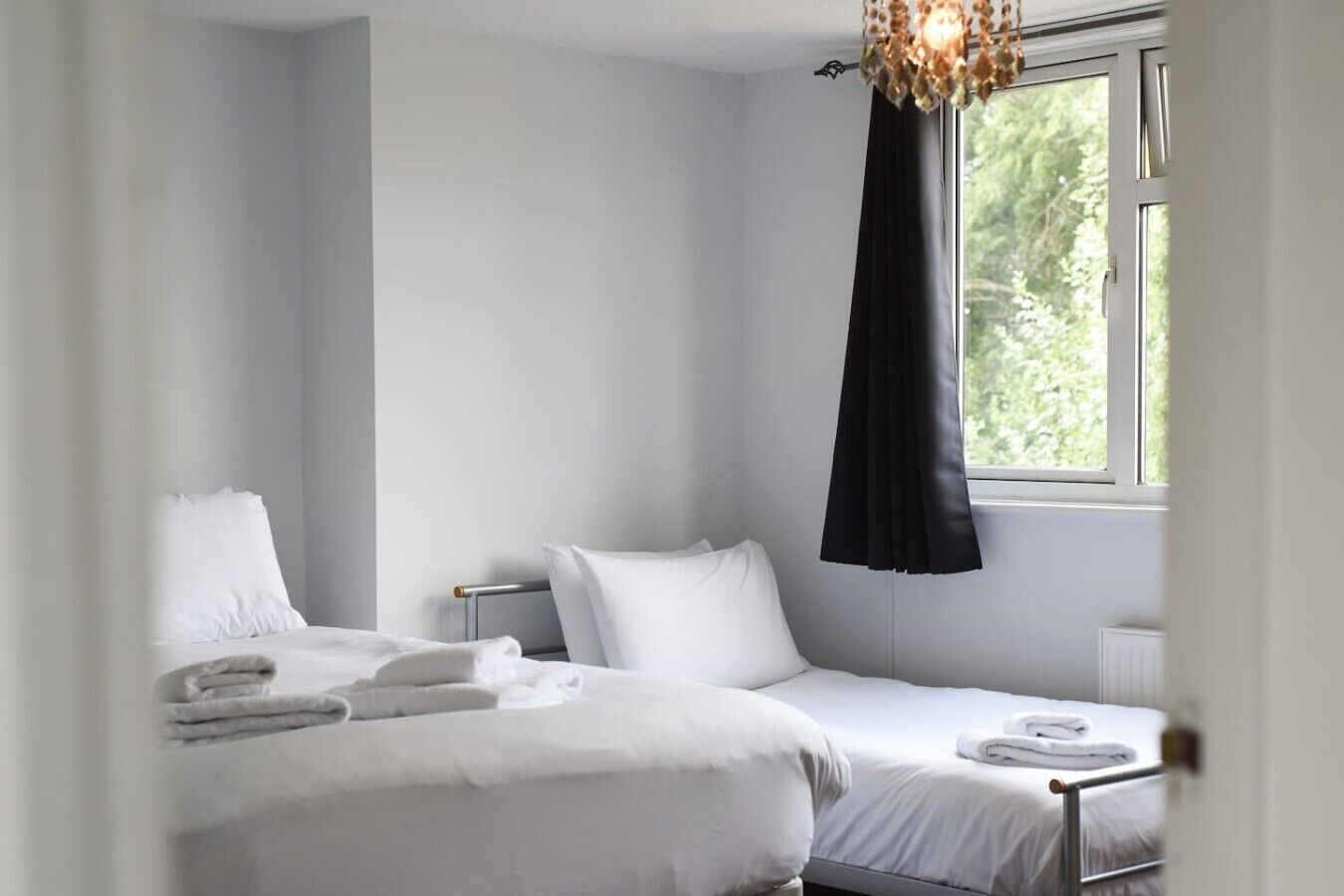 Een hotelkamer met twee bedden, een raam met een zwart gordijn en een kroonluchter.