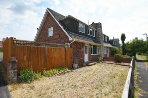 A two-story house with a brick exterior, a wooden fence, and a gravel driveway. - Spacious 4-Bedrooms and 6 Beds Home | Free Parking | Ideal for Contractors & Families (Hampshire)