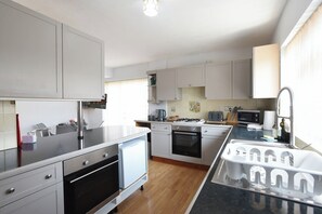 A modern kitchen with white cabinets, a black countertop, a built-in oven, a microwave, and a sink with a faucet. - Spacious 4-Bedrooms and 6 Beds Home | Free Parking | Ideal for Contractors & Families (Hampshire)