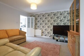 A living room with a sofa, a television, a cabinet, and a patterned wall. - Spacious 4-Bedrooms and 6 Beds Home | Free Parking | Ideal for Contractors & Families (Hampshire)