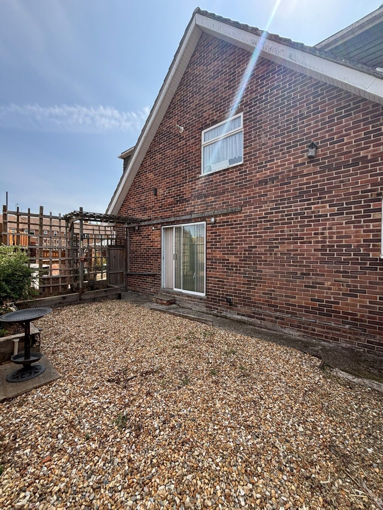 A brick building with a sloped roof, a wooden fence, and a gravel patio.