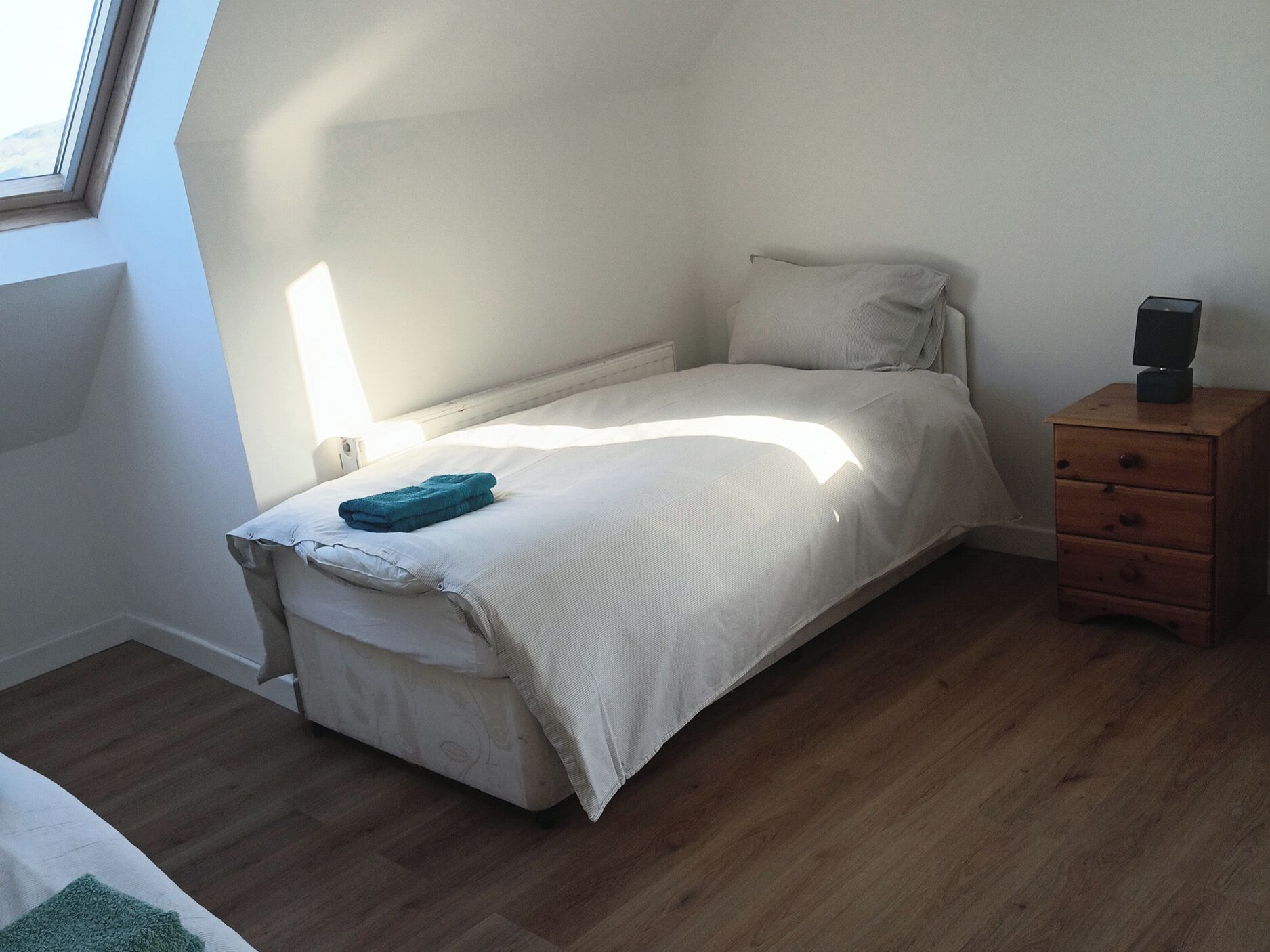 Une chambre à coucher avec un lit, une table de chevet, une lampe et une fenêtre.