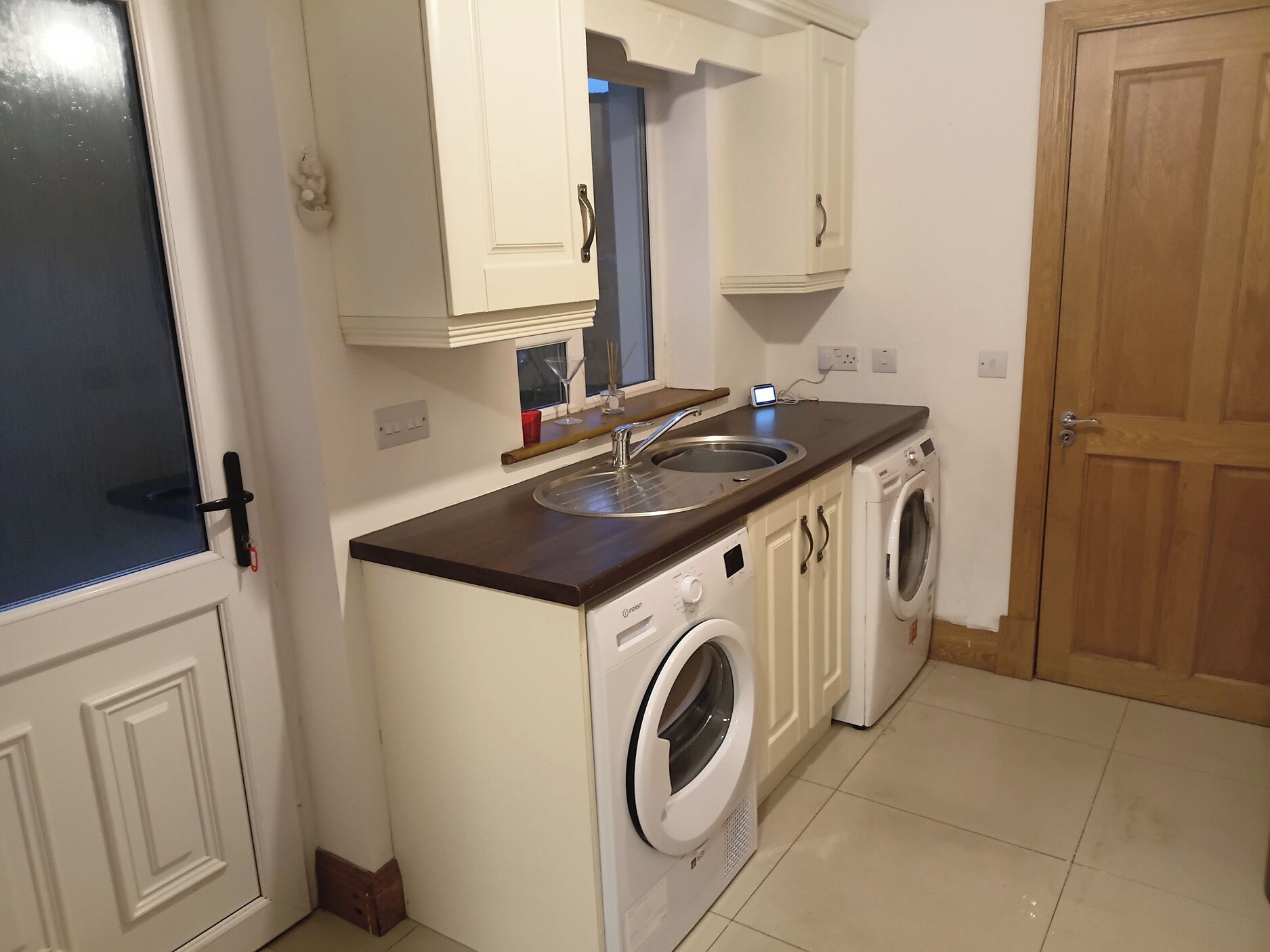 A compact kitchen with a sink, two white washing machines, and a wooden door.