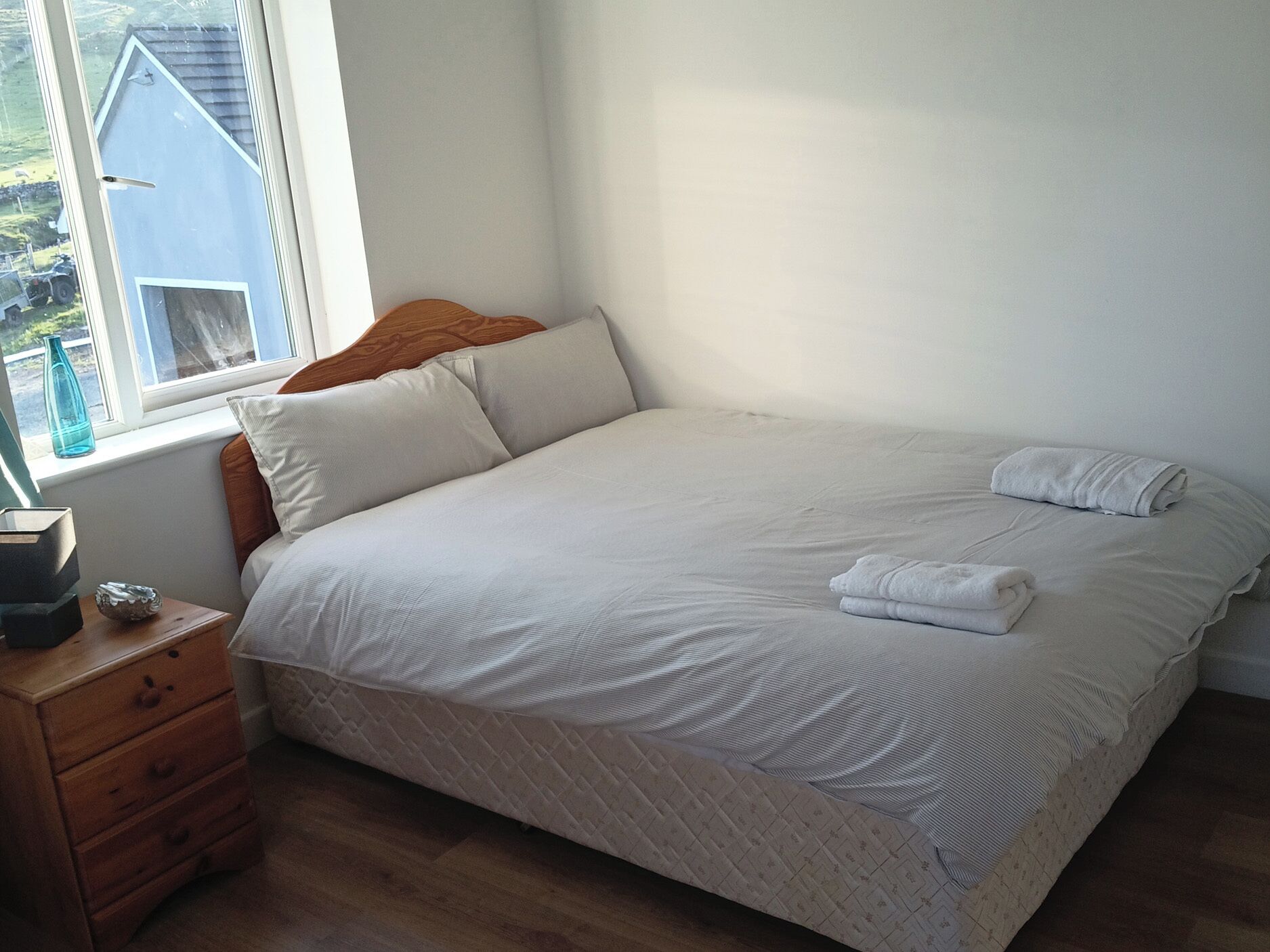 A bedroom with a large bed, a nightstand, a window, and a view of the outside.