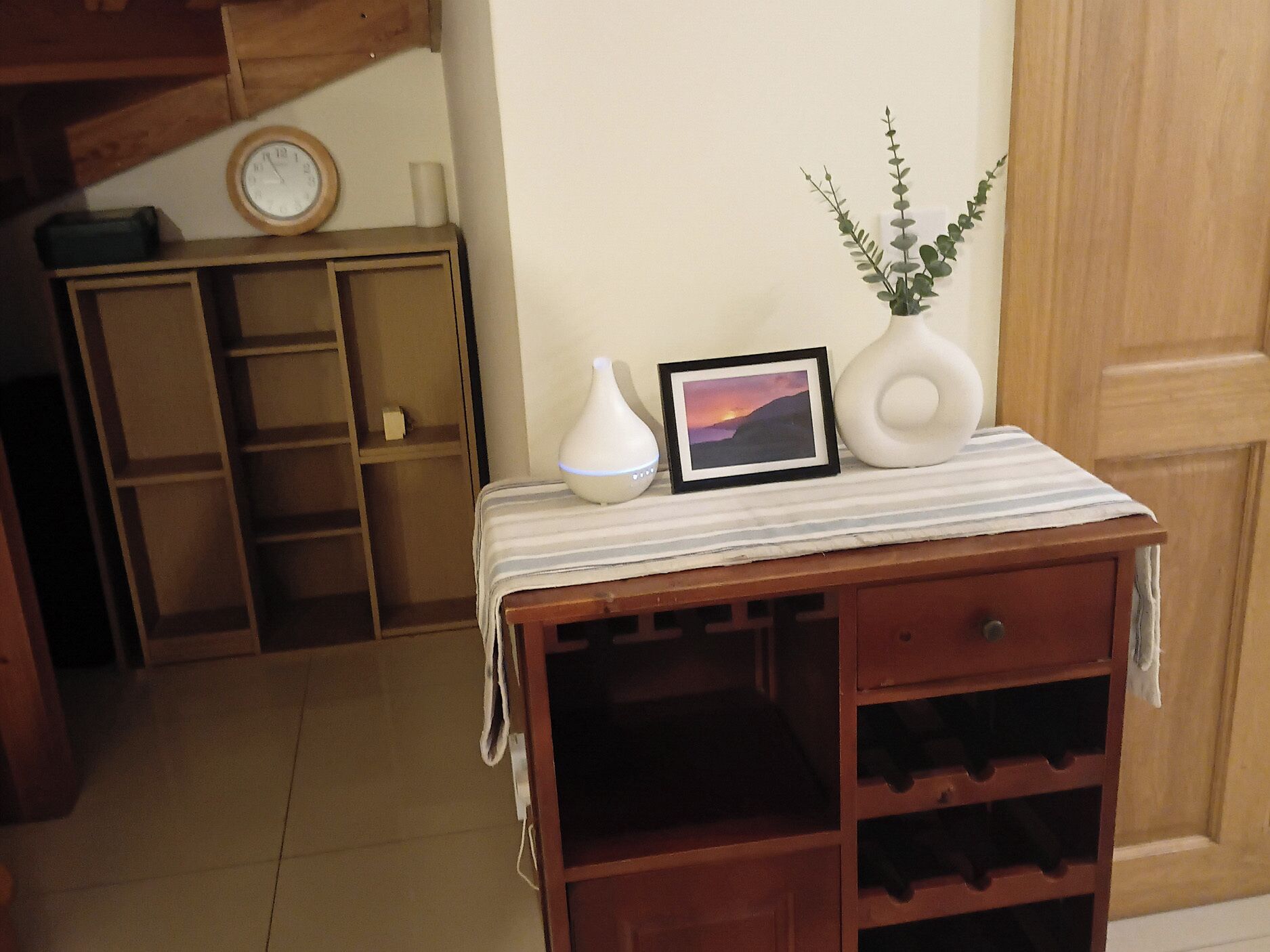 A wooden cabinet with a white vase and a framed picture on top.