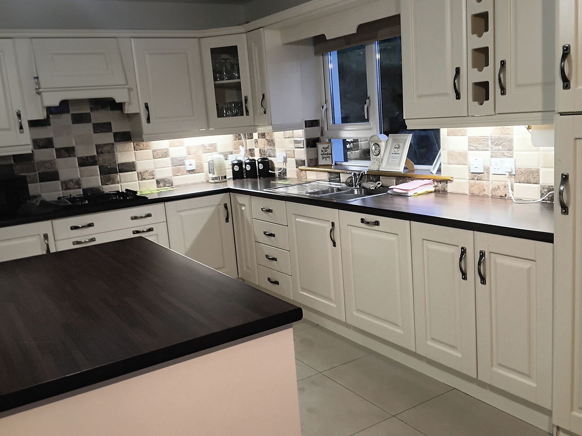 A modern kitchen with white cabinetry, a black countertop, and a window above the sink.
