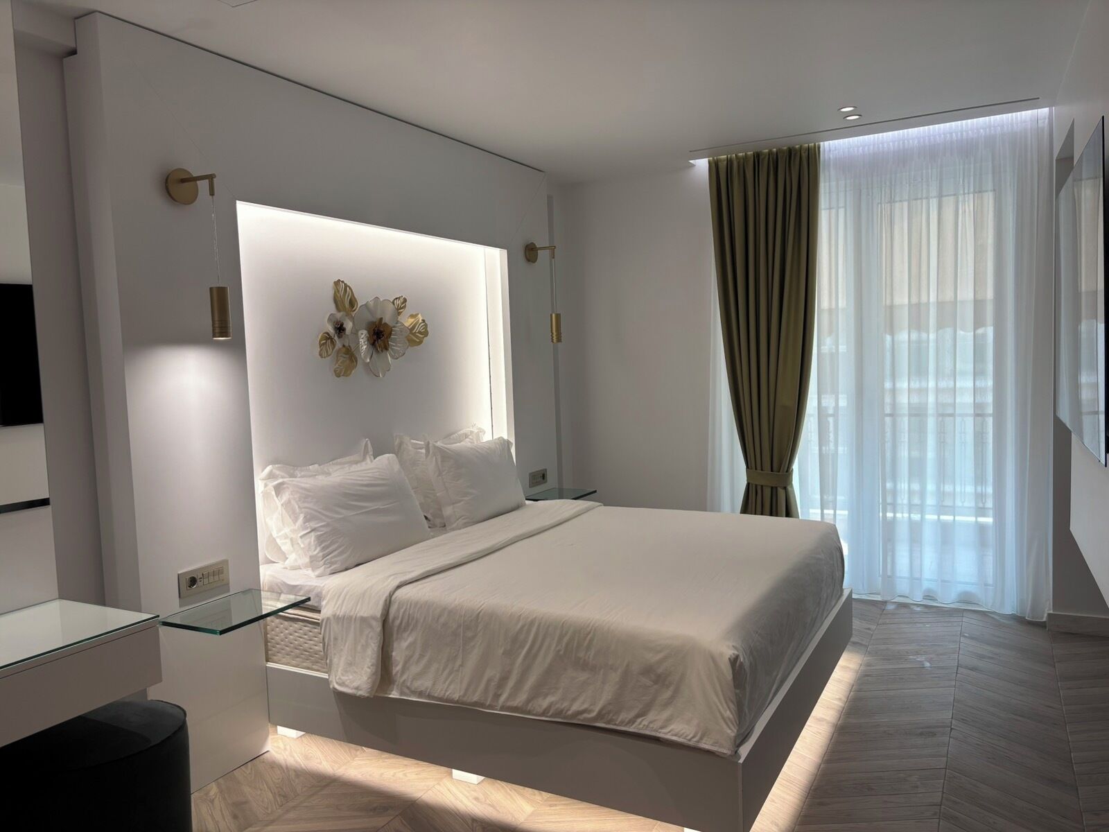 A modern bedroom with a large bed, bedside tables, a wall-mounted light, and a window with curtains.