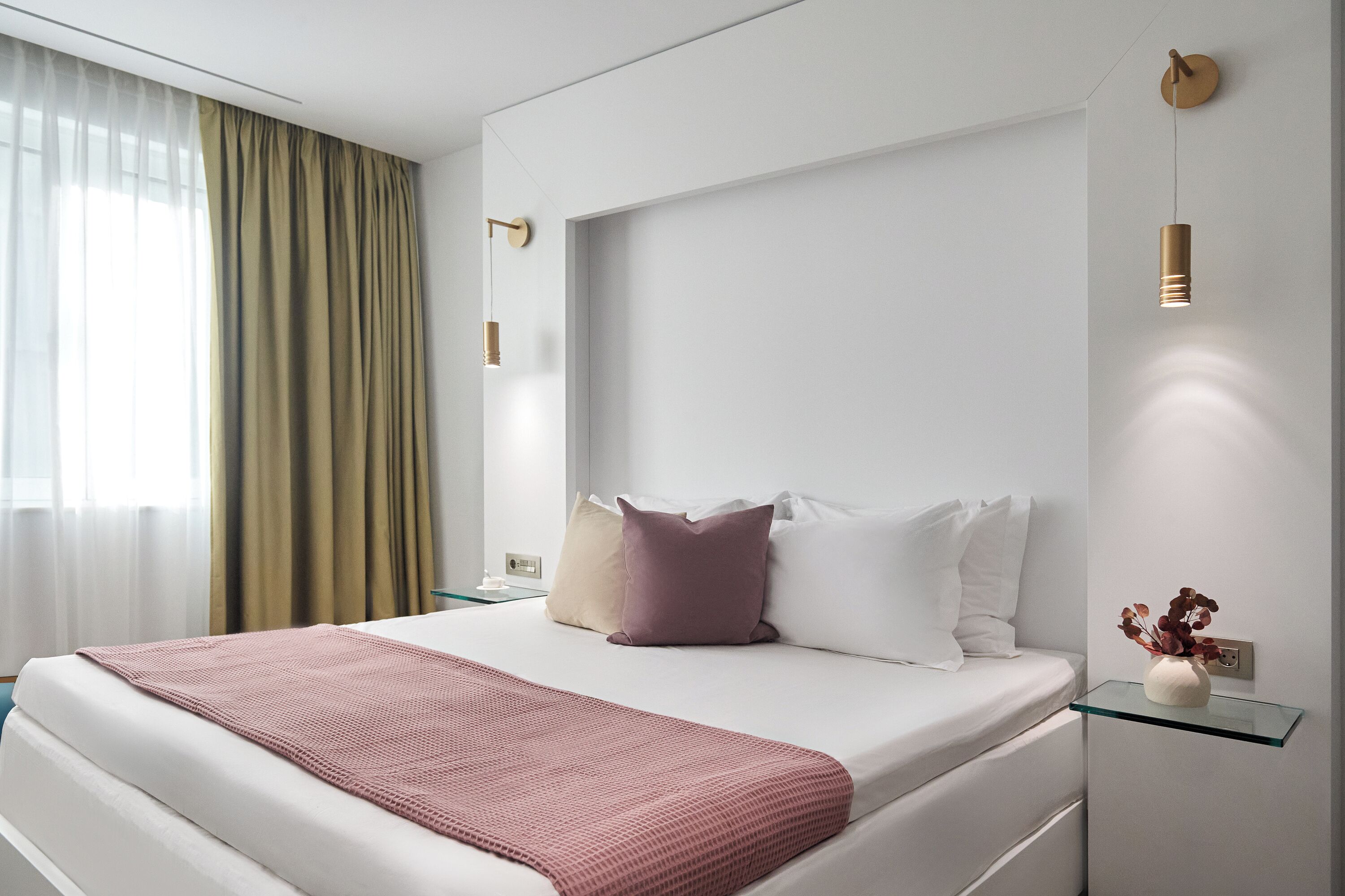 Une chambre d’hôtel moderne avec un grand lit, une table de chevet ornée d’un vase et un luminaire fixé au mur.