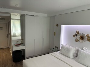 A hotel room with a bed, a bedside table, a mirror, a wardrobe, and a wall-mounted light fixture. - WHITE ROSE ATHENS RESIDENCE (Athens)