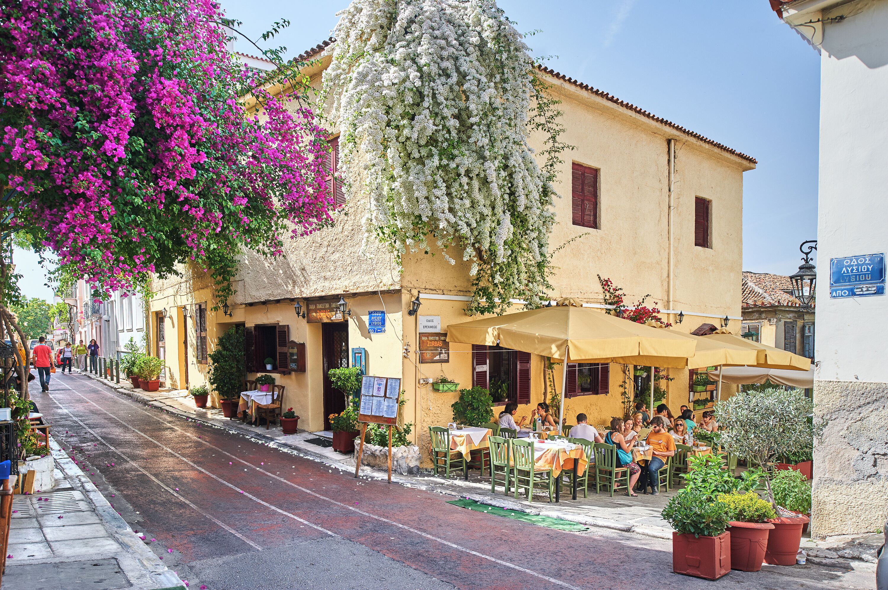 A street with a café, outdoor seating, and a building with a sign.