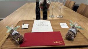 A wooden table with a red folder, two wine bottles, two wine glasses, and a welcome card. - WHITE ROSE ATHENS RESIDENCE (Athens)