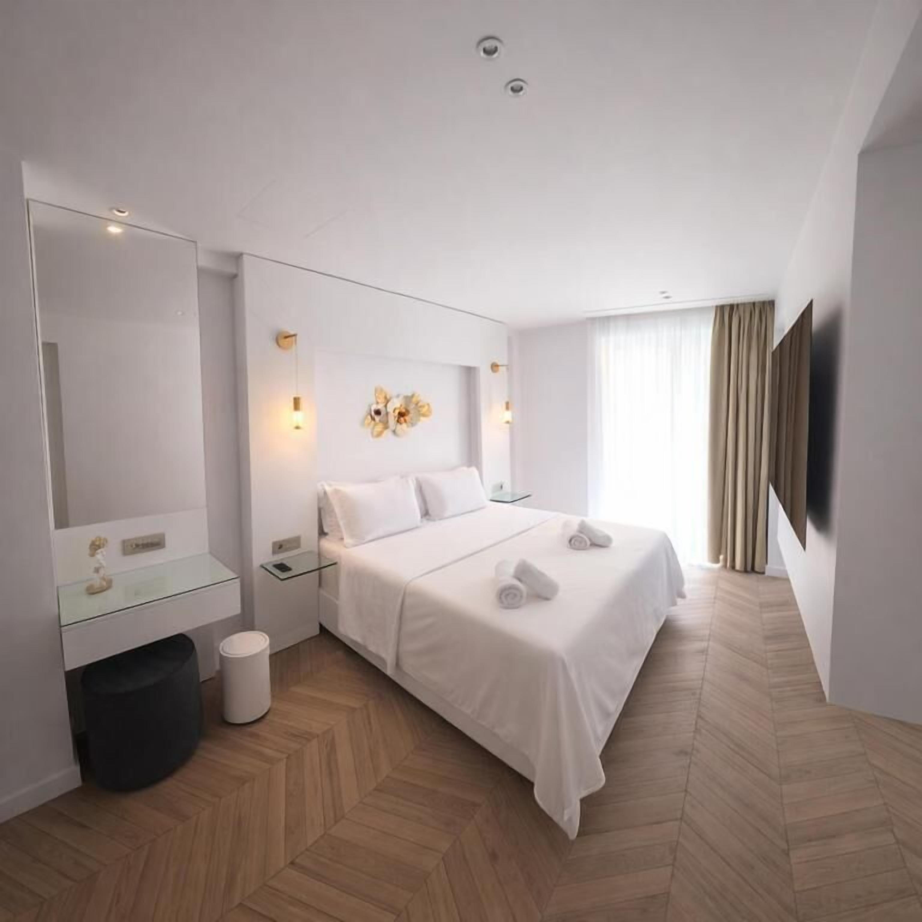 Une chambre d’hôtel avec un lit, des tables de chevet, un miroir, une télévision et une fenêtre avec des rideaux.