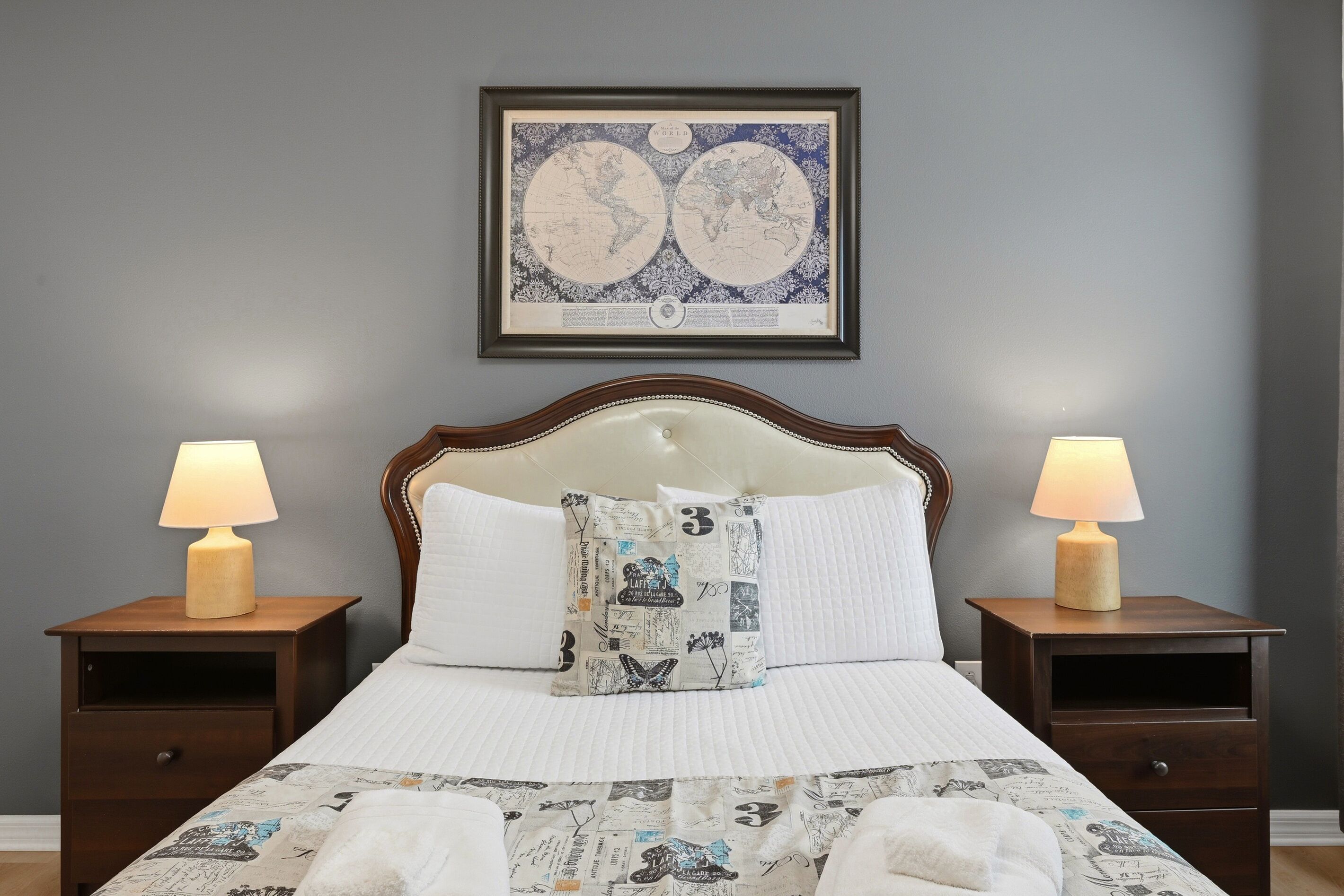 A bed with a quilted cover, two bedside tables with lamps, and a framed world map on the wall.
