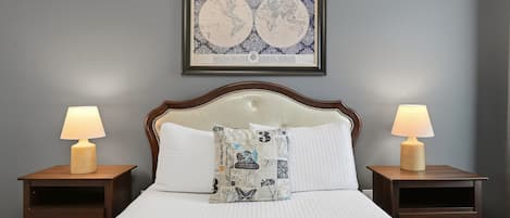 A bed with a quilted cover, two bedside tables with lamps, and a framed world map on the wall.
