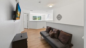 A modern living room with a grey sofa, wooden flooring, a television mounted on the wall, and a decorative wall piece. - Modern 6BRPoolVilla w/HotTub &GameRoom Near Disney (Kissimmee)