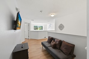 A modern living room with a grey sofa, wooden flooring, a television mounted on the wall, and a decorative wall piece. - Modern 6BRPoolVilla w/HotTub &GameRoom Near Disney (Kissimmee)